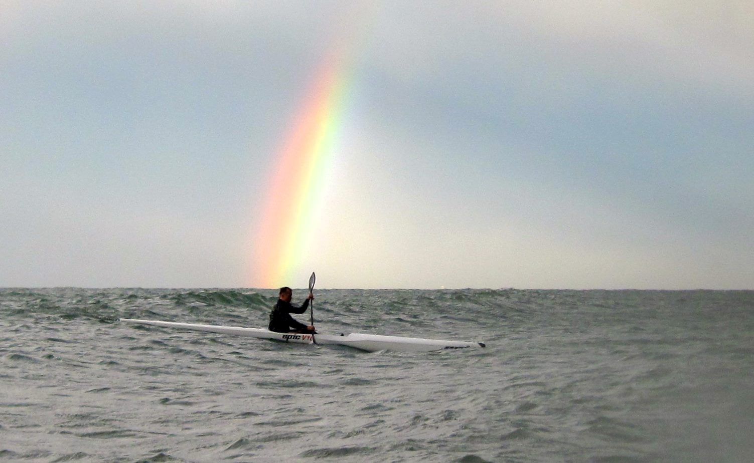 en surfkajak der ror og man kan se en regnbue